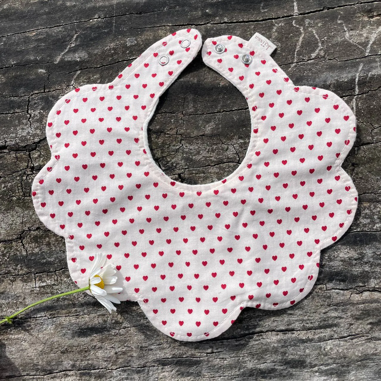 A flower-shaped Kiissa bib in white cotton with tiny red hearts