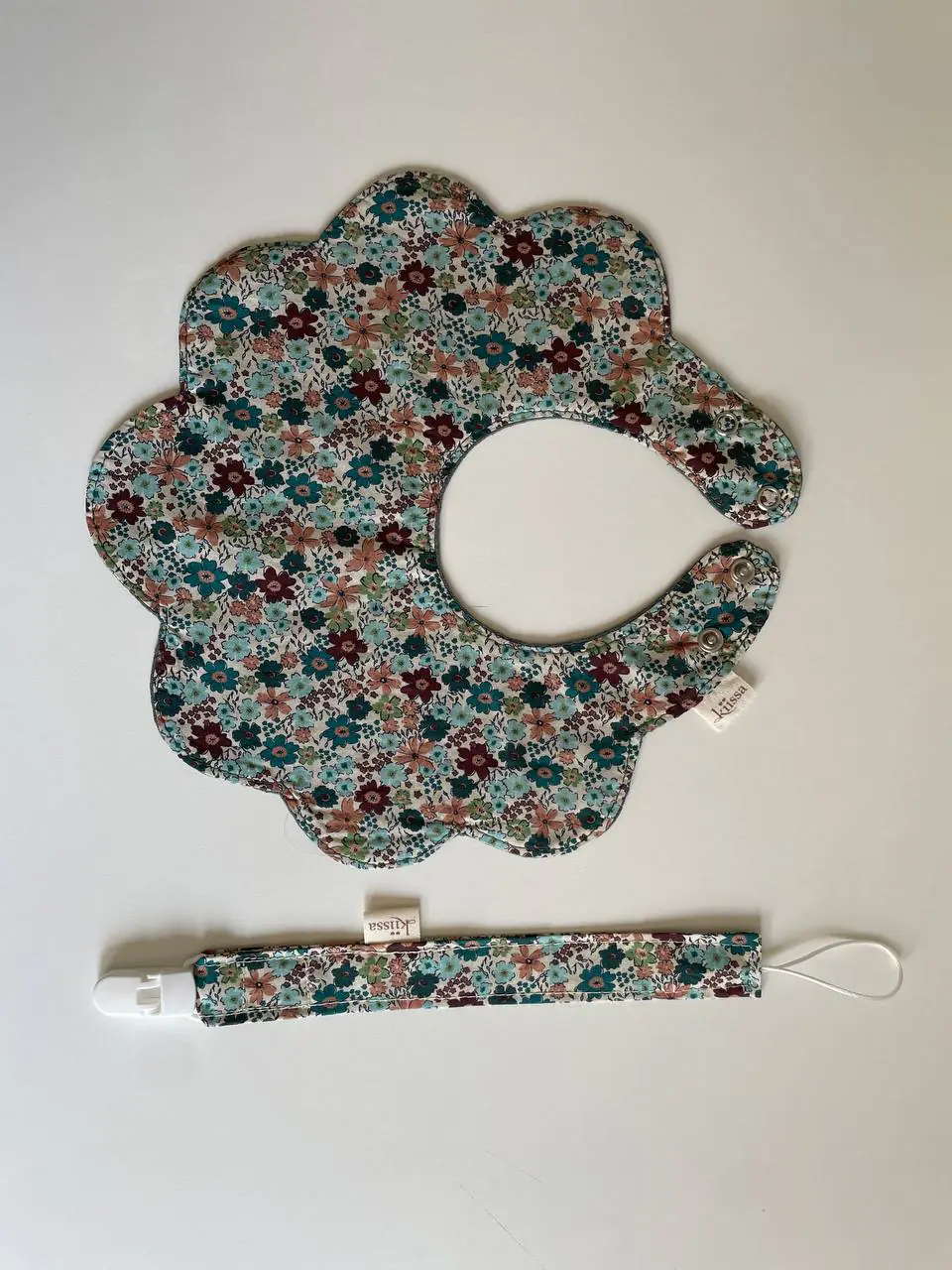 A floral bib and pacifier clip arranged together