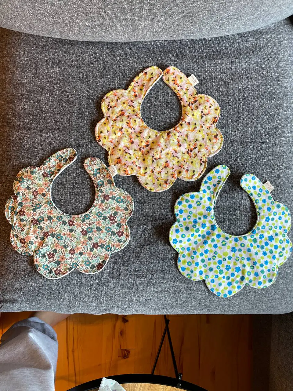 Three handmade bibs resting on a grey sofa