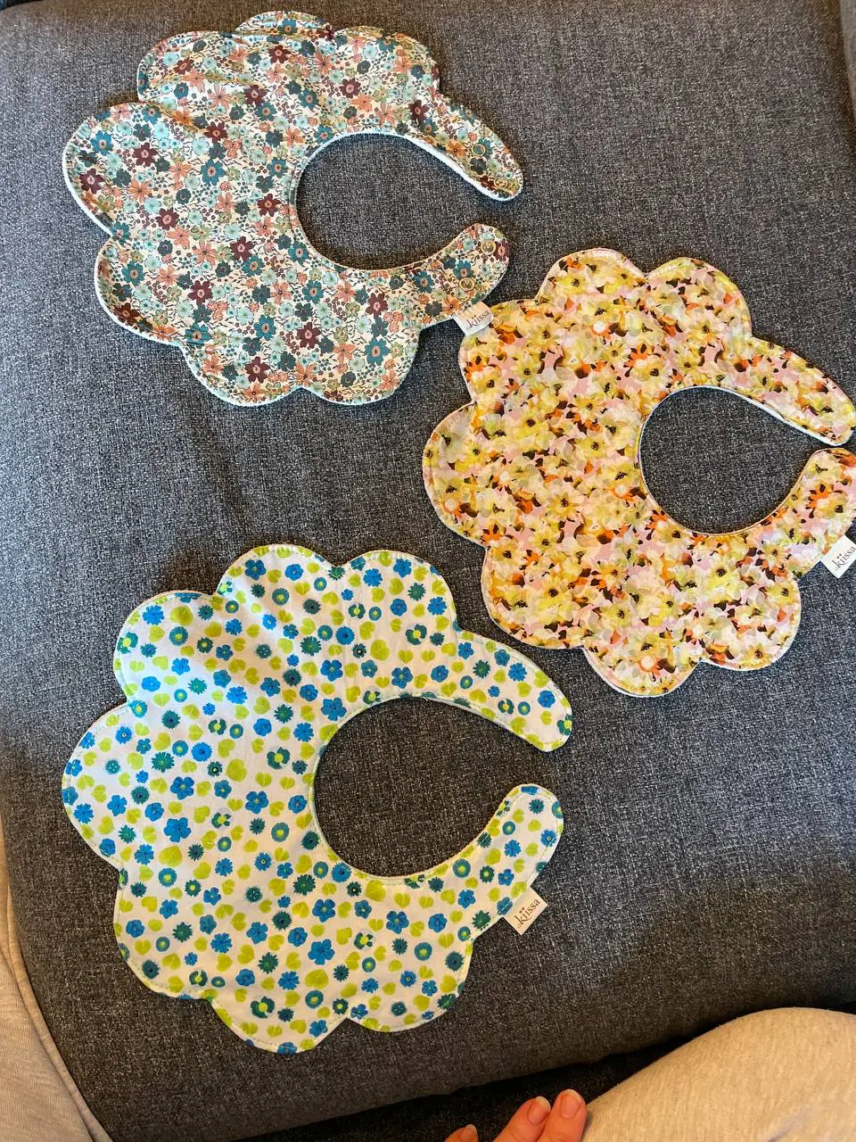 Three bibs overlapping on a grey sofa